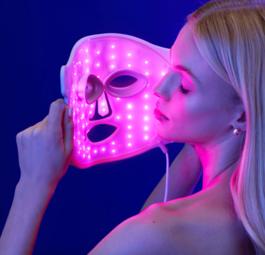 A woman holding a red light therapy mask.