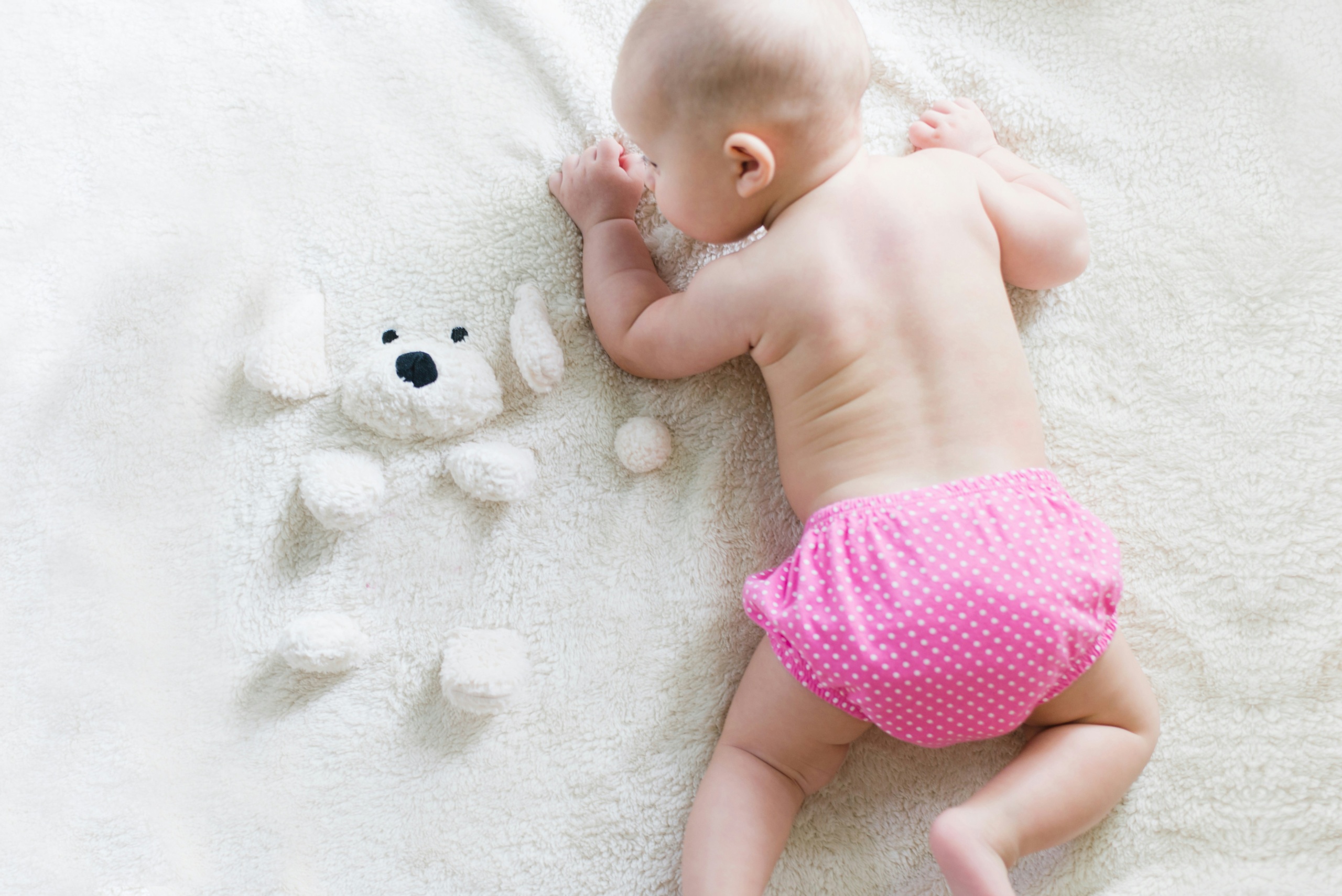 A baby crawling on a soft white blanket.
