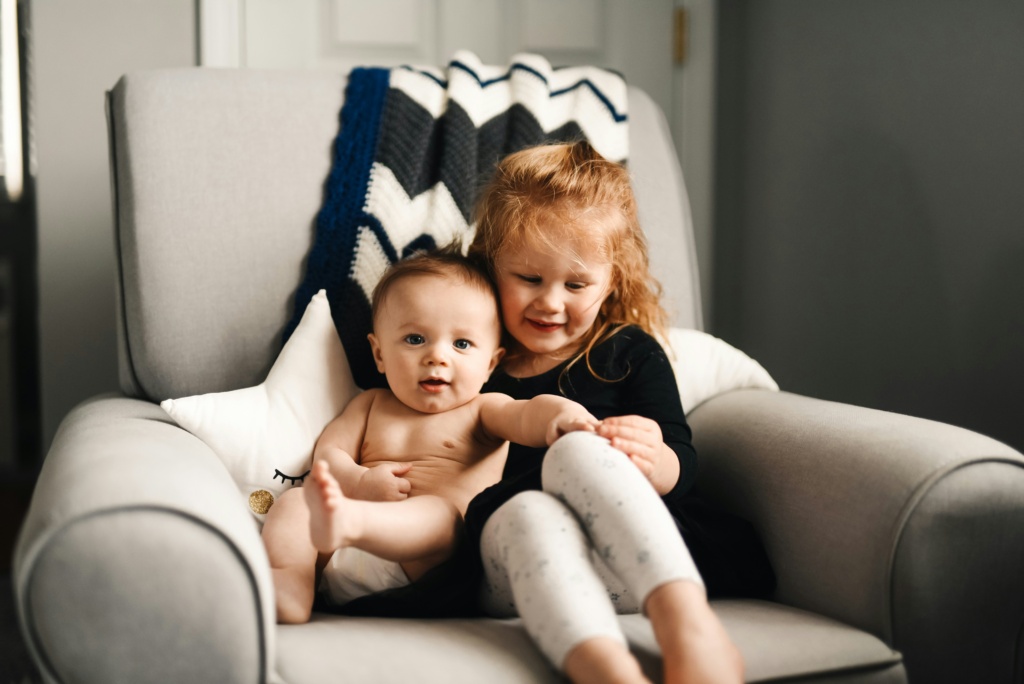 A baby and a toddler sitting on an armchair.