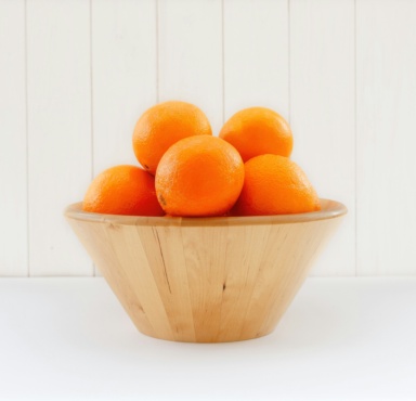 A wooden bowl full of oranges.