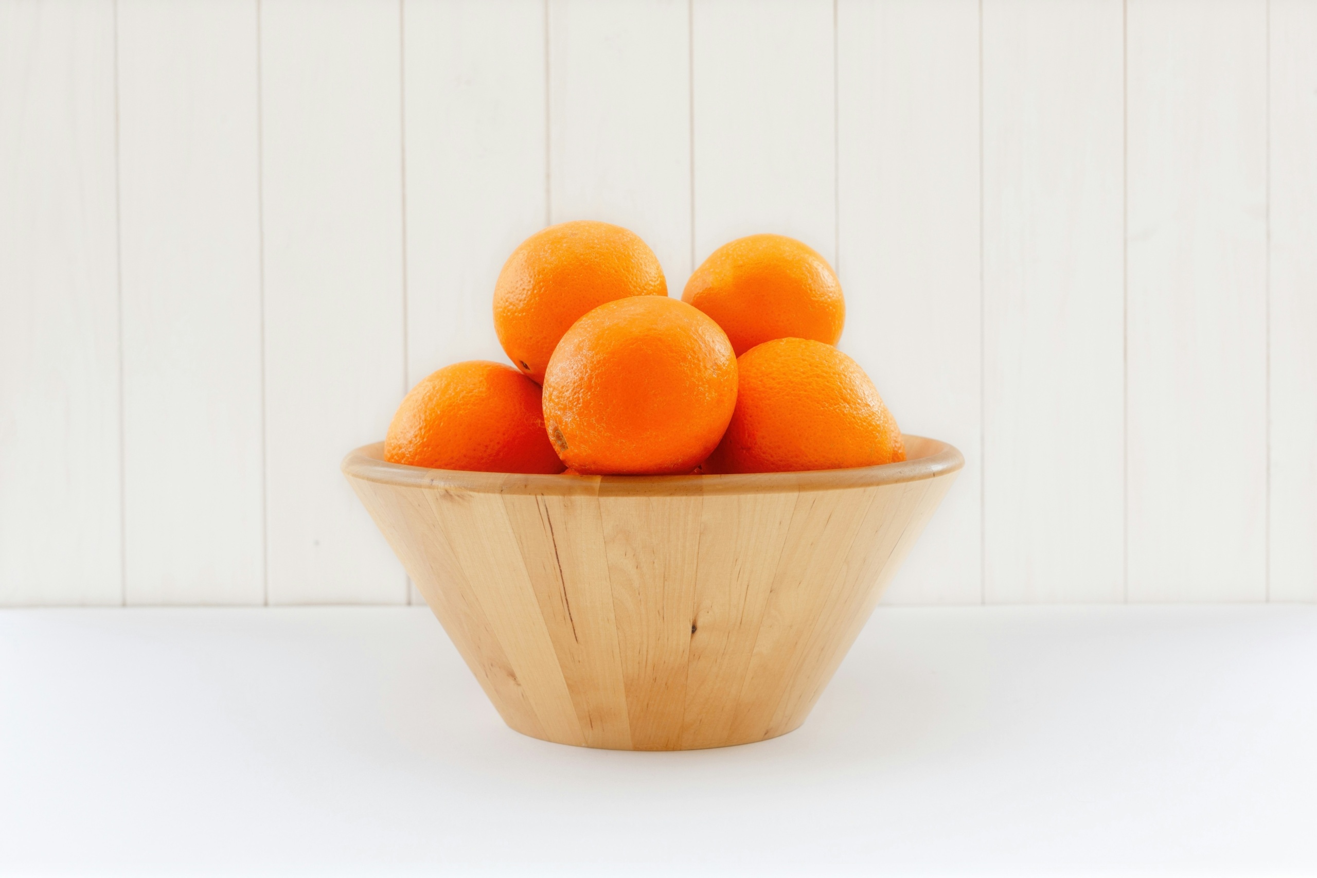 A wooden bowl full of oranges.